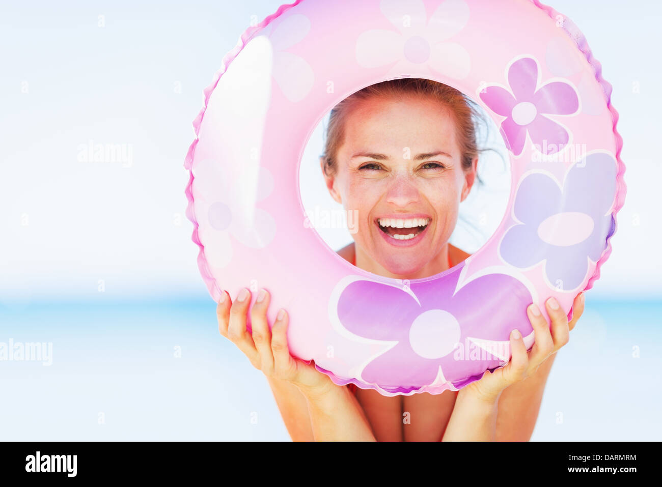 Smiling young woman on beach looking through swim ring Stock Photo Alamy