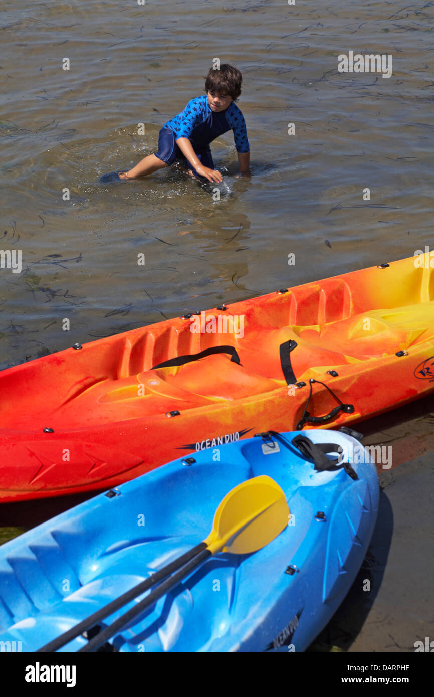 young boy in the sea with colourful kayaks at Sandbanks, Poole, Dorset in July Stock Photo