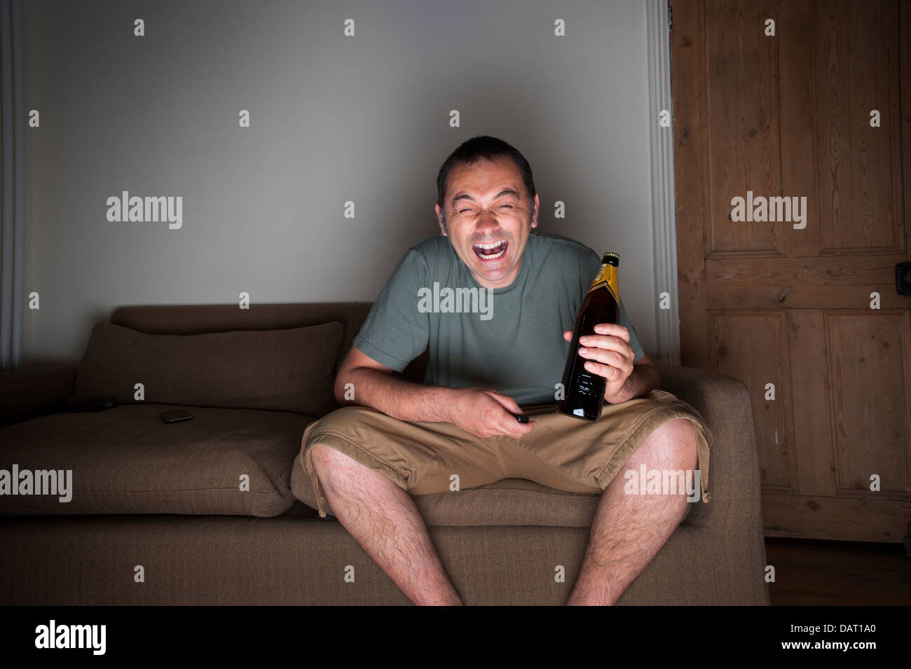 man drinking beer and laughing at the television or tv Stock Photo