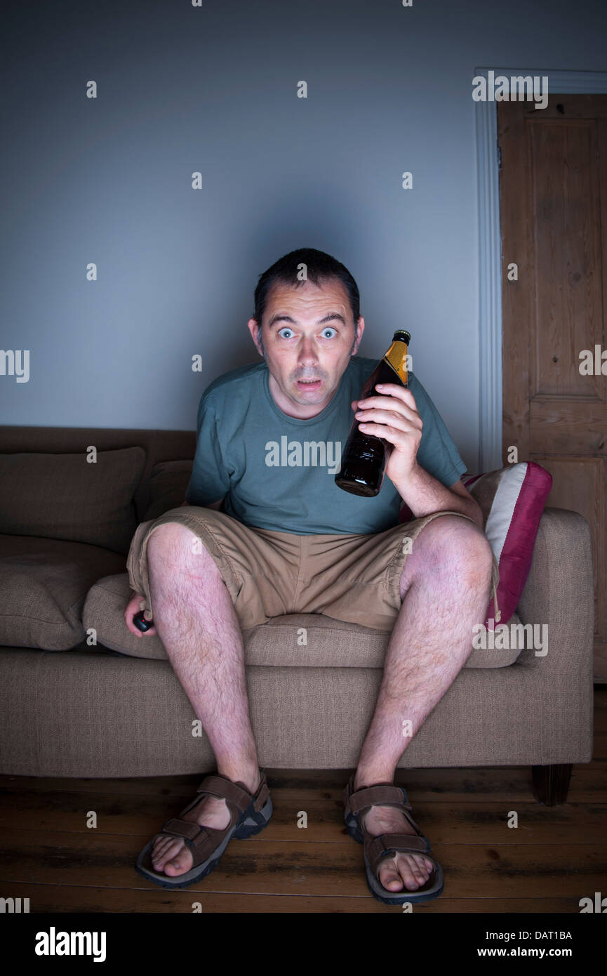 man watching tv or television in disbelief drinking beer Stock Photo