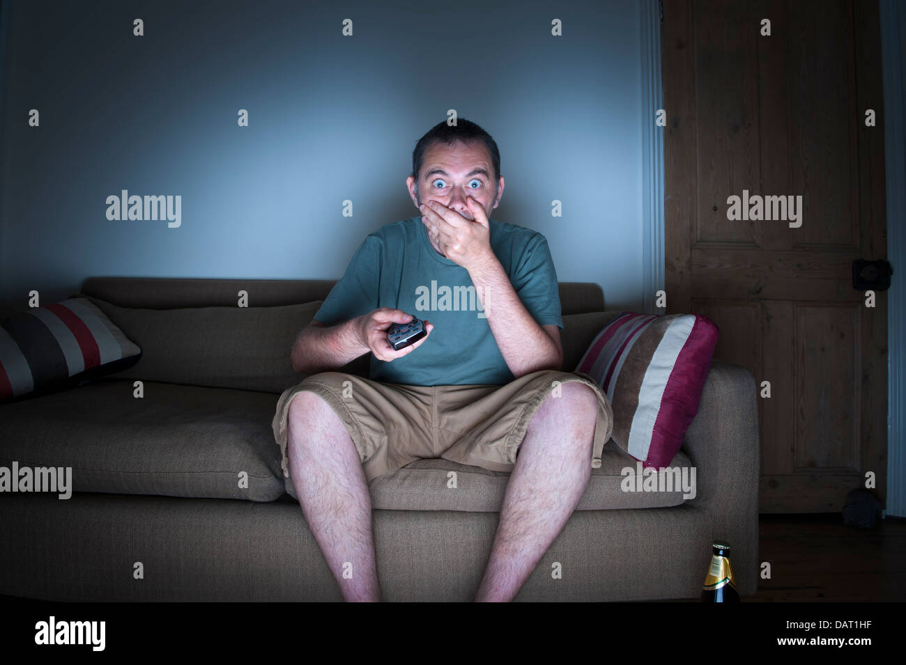 man covering mouth watching tv or television in disbelief Stock Photo