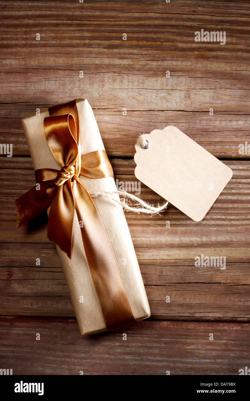 Brown rectangular present box on a rustic wood table with a bow and a blank label Stock Photo
