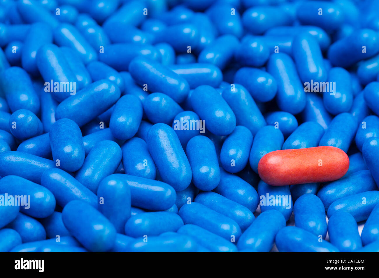 Close shoot of one red drug pill laying on many blue tablets Stock Photo