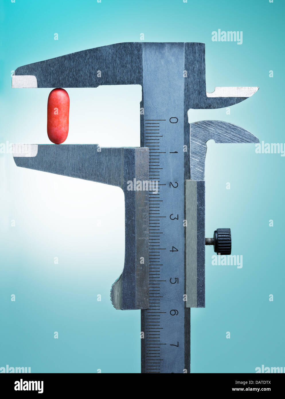 Vernier caliper measures size of red pill, on blue Stock Photo