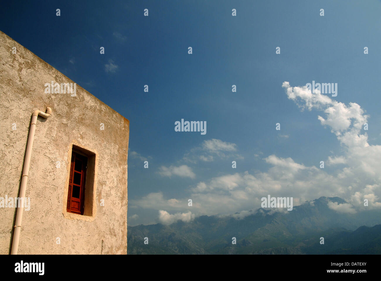 Small building in a hill-side village in Corsica, France. Mountains and blue sky on horizon. Stock Photo