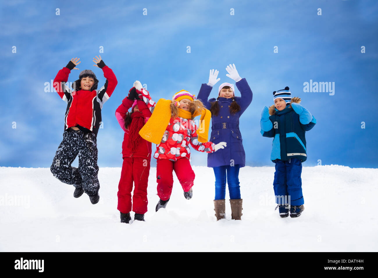 Group of five happy kids jumping in snow with lifted hands Stock Photo