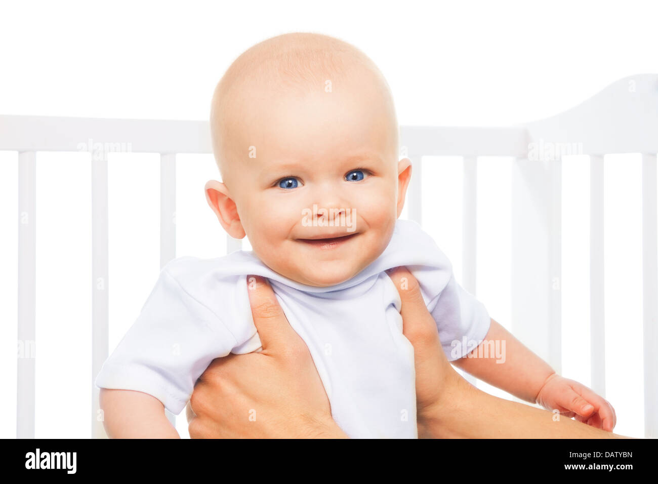 Cute little baby boy lifted in parents hands in his crib, isolated on