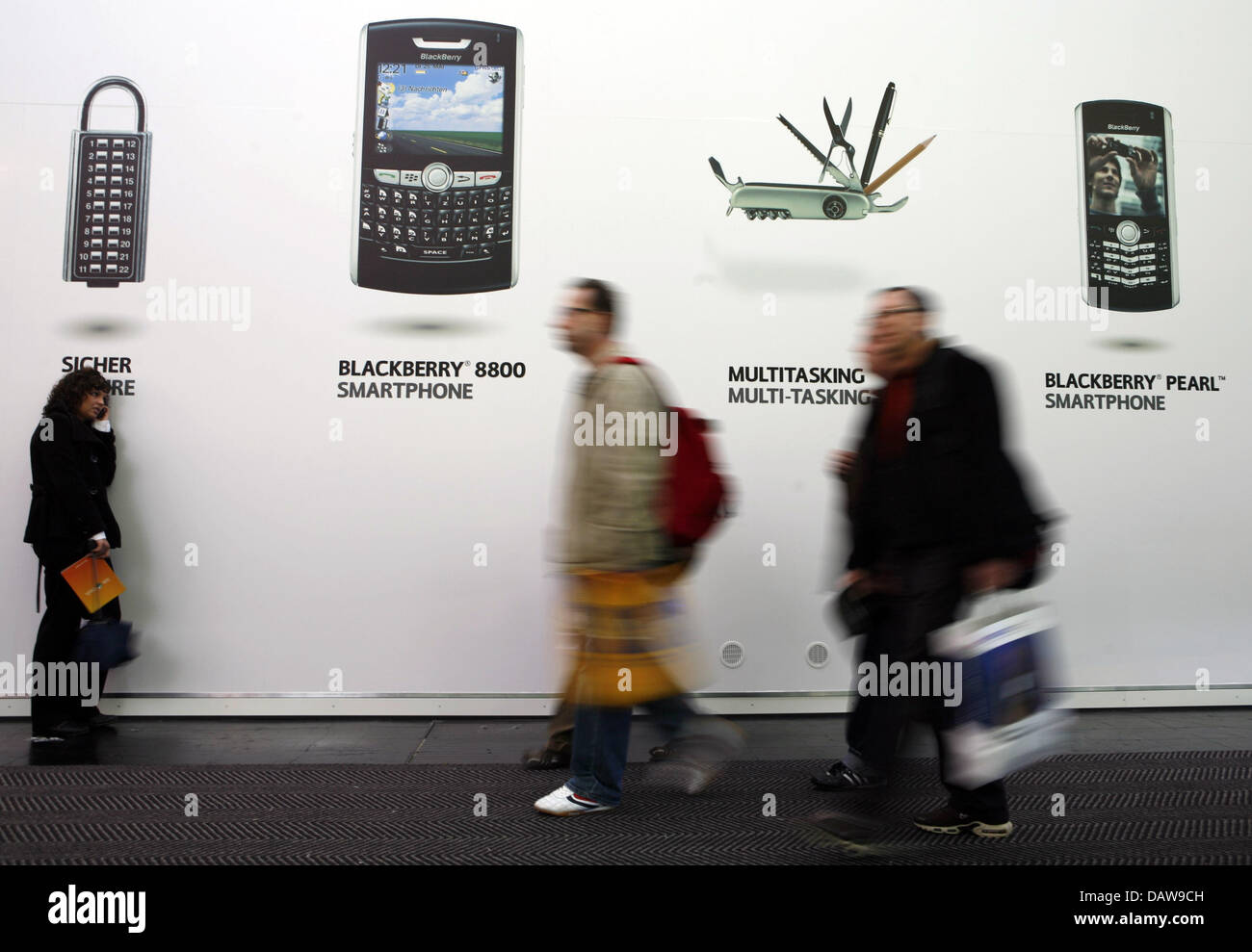 Visitor walk past an advertisement poster of cell phone suppliers at the 'CeBIT 2007' trade fair in Hanover, Germany, Saturday 17 March 2007. It is the world's largest trade fair showcasing digital IT and telecommunications solutions for home and work environments and runs from 15th until 21st March 2007. More than 6,000 companies from 77 countries will exhibit their latest digital Stock Photo