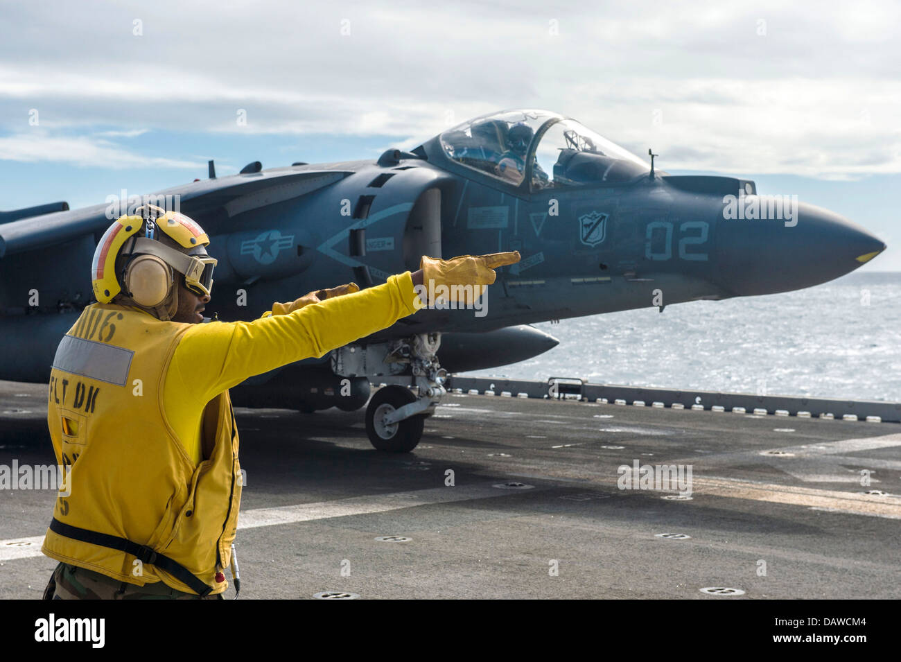 A US Navy Aviation Boatswains Mate signals to the pilot of an AV-8B Harrier fighter aircraft that he is cleared for launch from the flight deck of the amphibious assault ship USS Bonhomme Richard July 16, 2013 in the Coral Sea. Stock Photo
