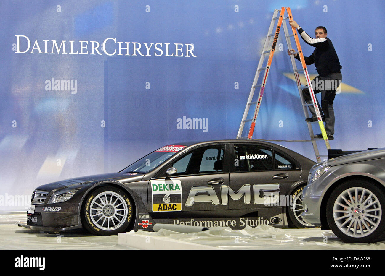 A worker cleans a 'DaimlerChrysler' advertising poster behind a Mercedes  C-Class tuned by AMG in preparation of the 17th AMI (AutoMobile  International) Leipzig motor show on the trade fair compounds in Leipzig,