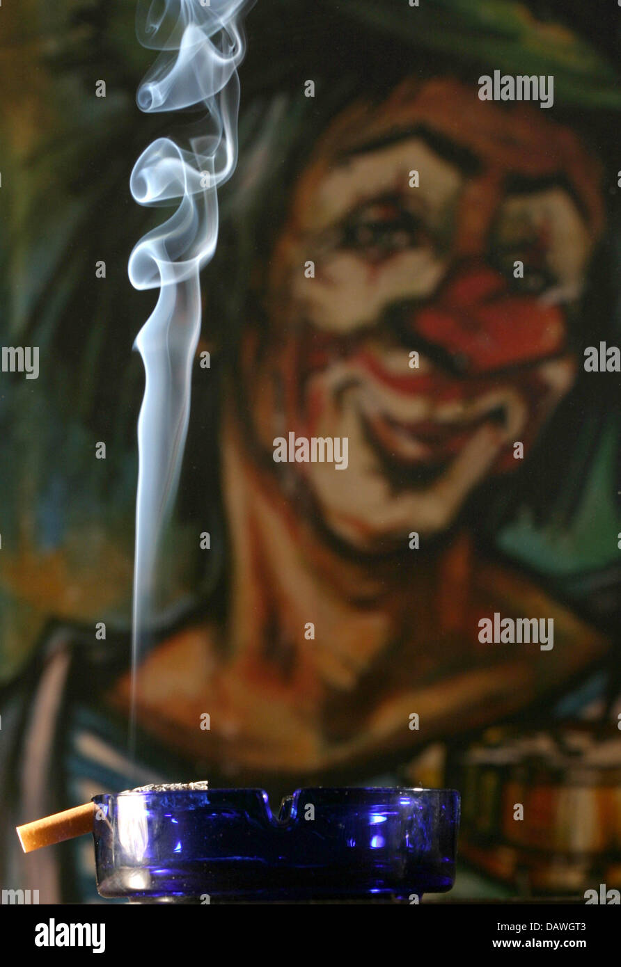 A smoking cigarette is pictured in an ashtray in front of a clown's placard  in Frankfurt Main, Germany, 18 December 2006. Photo: Tobias Felber Stock  Photo