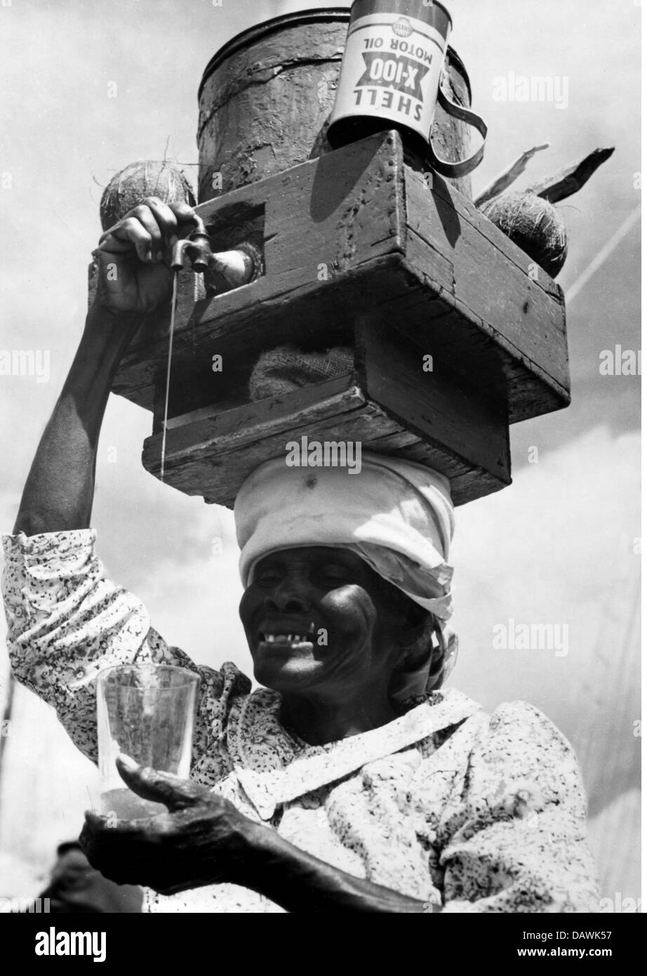 oddity, African woman with water barrel on her head, pouring water overhead into glass, 1960s, Additional-Rights-Clearences-Not Available Stock Photo