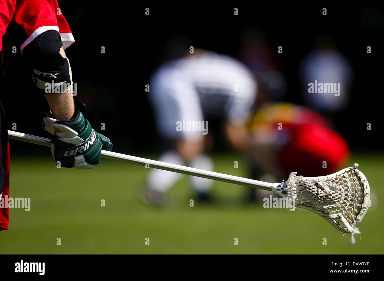 A Lacrosse player holds his crosse while the referee places the ball in
