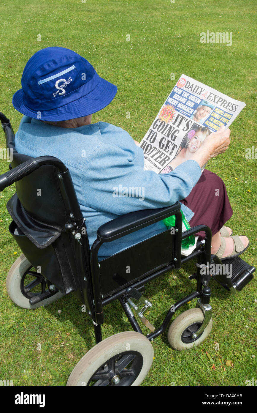 90 year old woman wearing light clothing to protect from sun reading heatwave warning on front page of Daily Express. UK Stock Photo