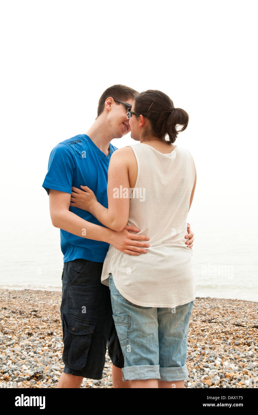 A young couple in their late teens or early twenties hugging and about to kiss on a beach Stock Photo
