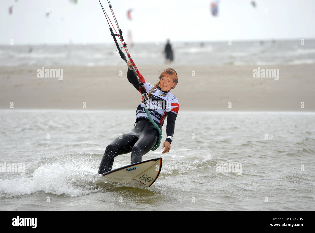 St. Peter-Ording, Germany. 19th July, 2013. Ninefold kitesurf world champion Kristin Boese of Germany drives with a mask of chancellor Merkel at the Kitesurf World Cup 2013 in St. Peter-Ording, Germany, 19 July 2013. The World Cup is the biggest kit surfing event in the world. Chancellor Merkel is expected in St. Peter-Ording in the evening during her summer tour. Photo: MARCUS BRANDT/dpa/Alamy Live News Stock Photo