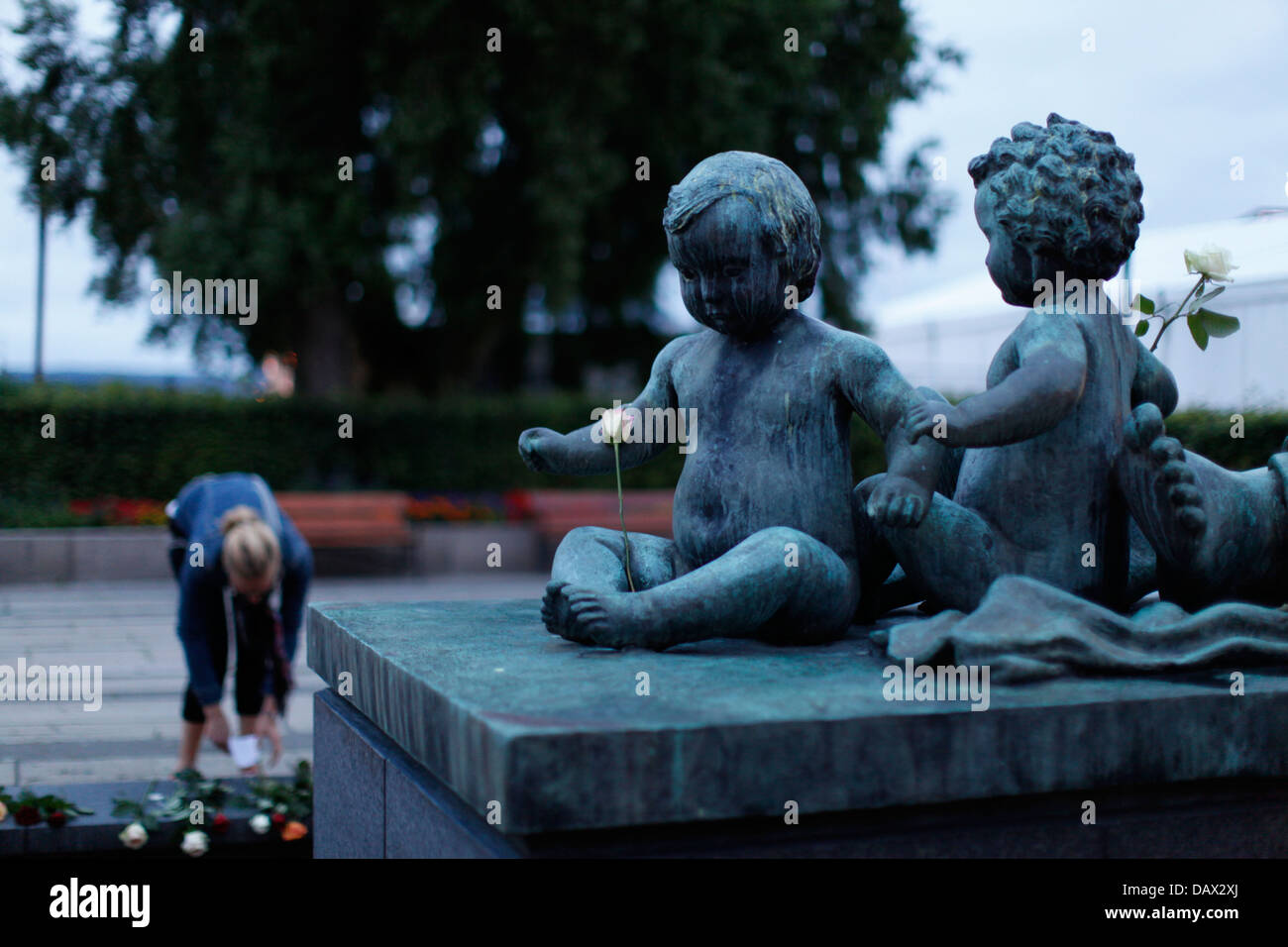 Girl putting down flowers in the background of a statue of two children with flowers. The day after the terrorist attack in Oslo and at Utoya Stock Photo