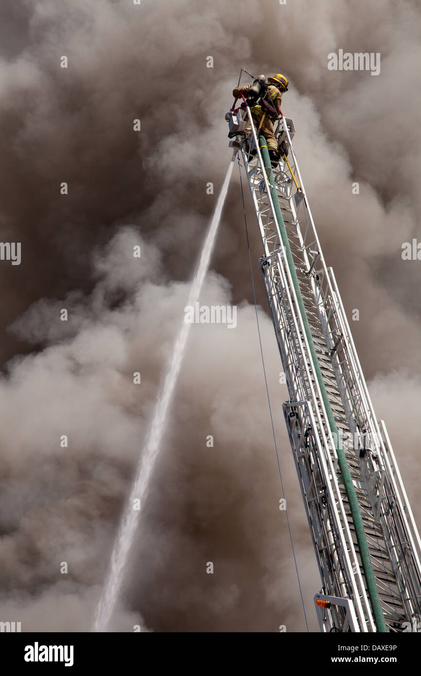 Firefighter on extended ladder sprays water on building fire Stock Photo