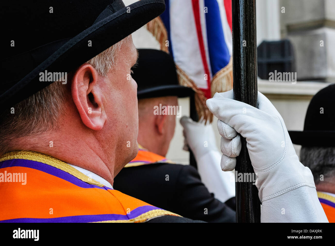 An Orangeman wearing an Orange sash and leather glove holds a flag pole Stock Photo
