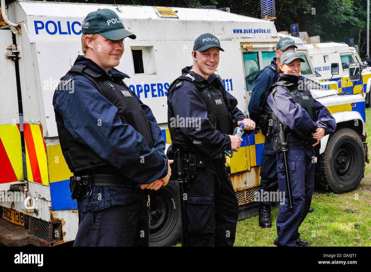 Police officers wearing bullet proof vests stand beside PSNI armoured Landrovers Stock Photo