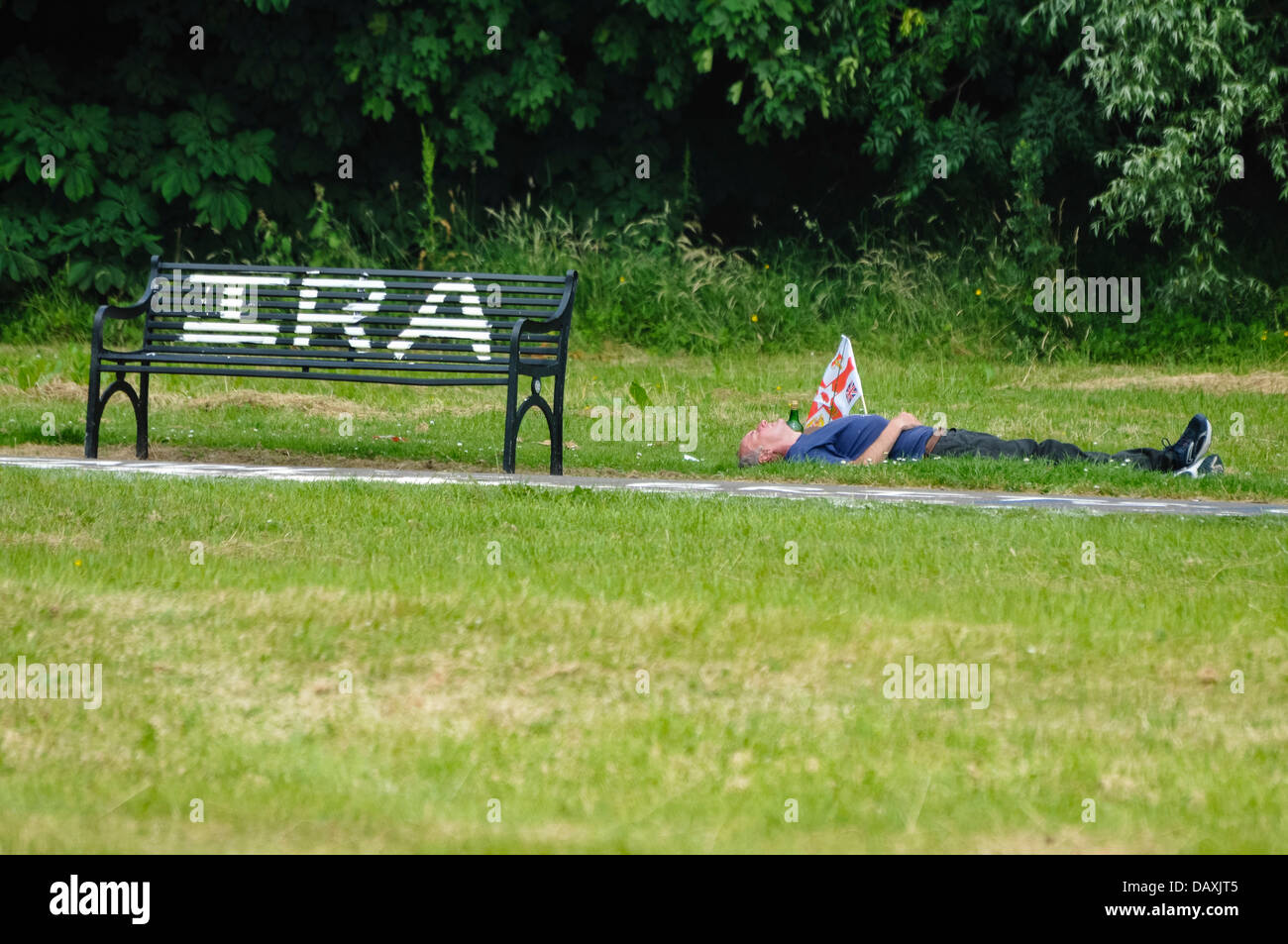 A drunk man with a Northern Ireland (Protestant) flag lies on the grass beside sectarian Republican grafitti Stock Photo