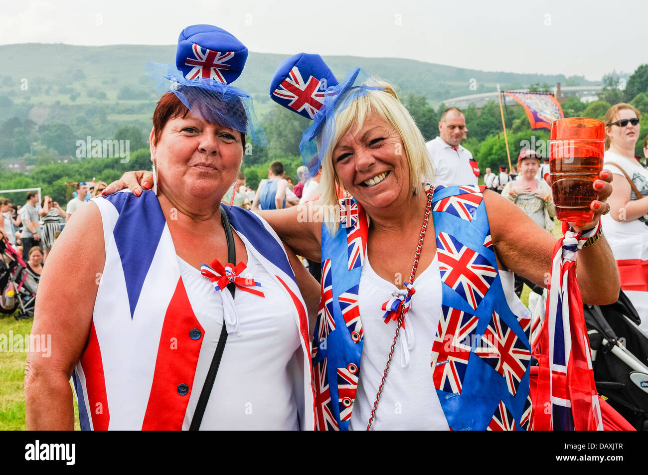 Two women watch the 12th July Orange Order parade wearing Union Flag clothing Stock Photo