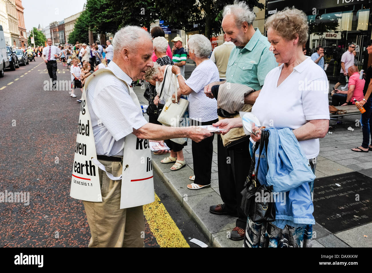 A man wearing a vest with bible verses hands out religious tracts to people in a crowd Stock Photo