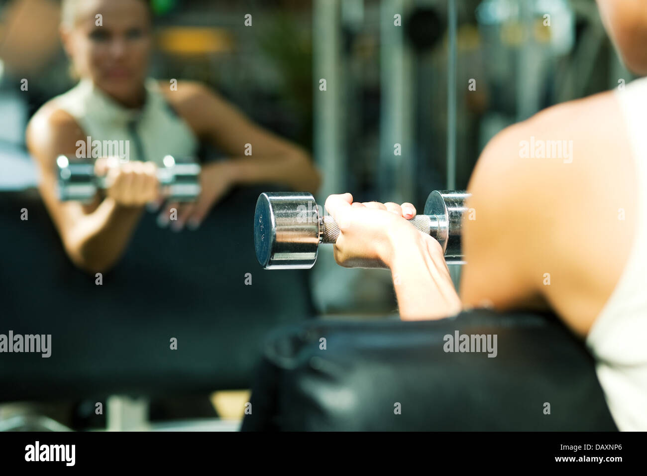 Woman lifting dumbbells in a gym, seeing herself in a mirror (focus only on the dumbbell) Stock Photo