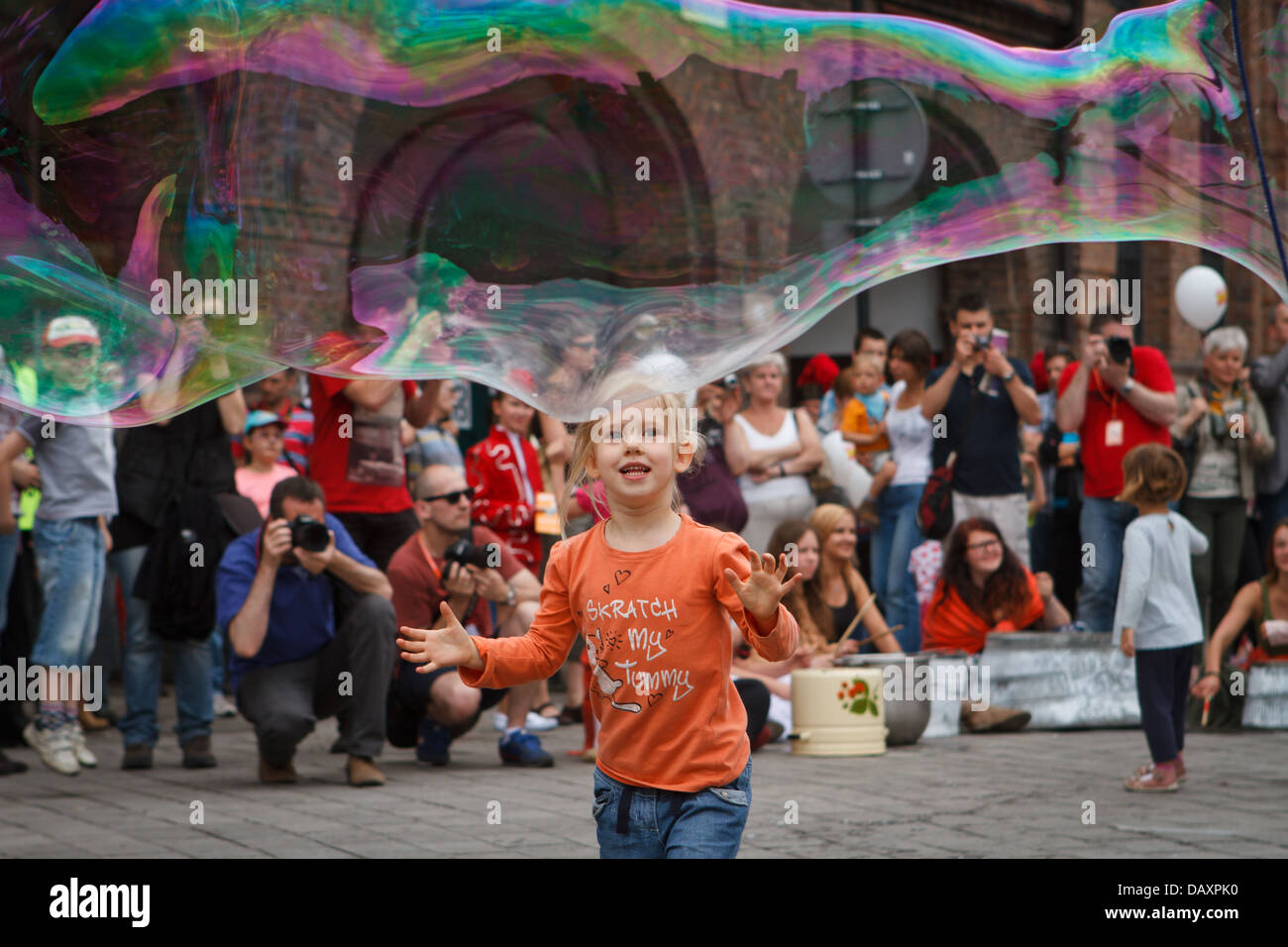 A girl catching big soap bubble during "Industriada" 2013 street performance at Nikiszowiec main square. Katowice, Poland. Stock Photo