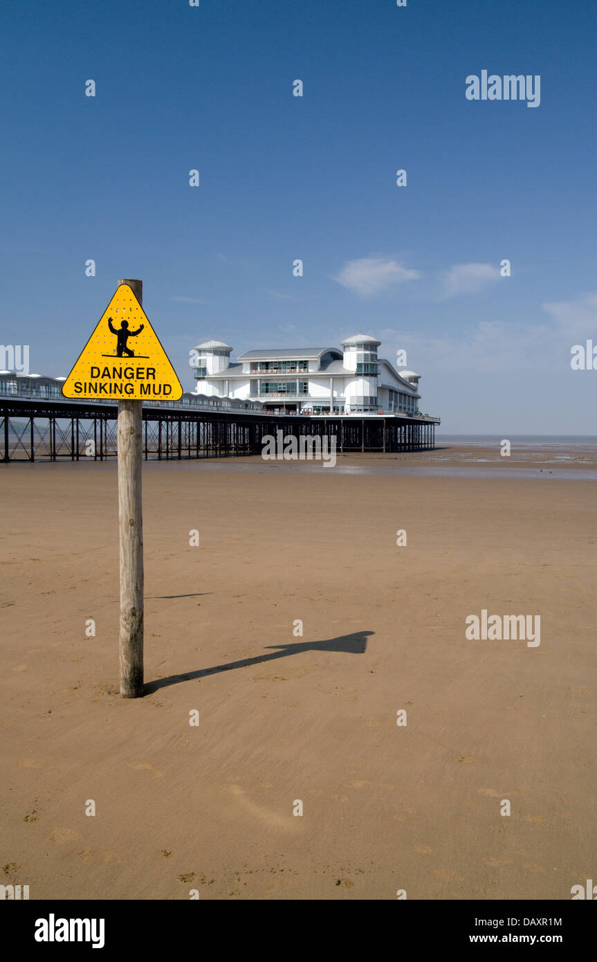 Sign warning of mud with the Grand Pier in the distance, Weston-Super-Mare, Somerset, England. Stock Photo