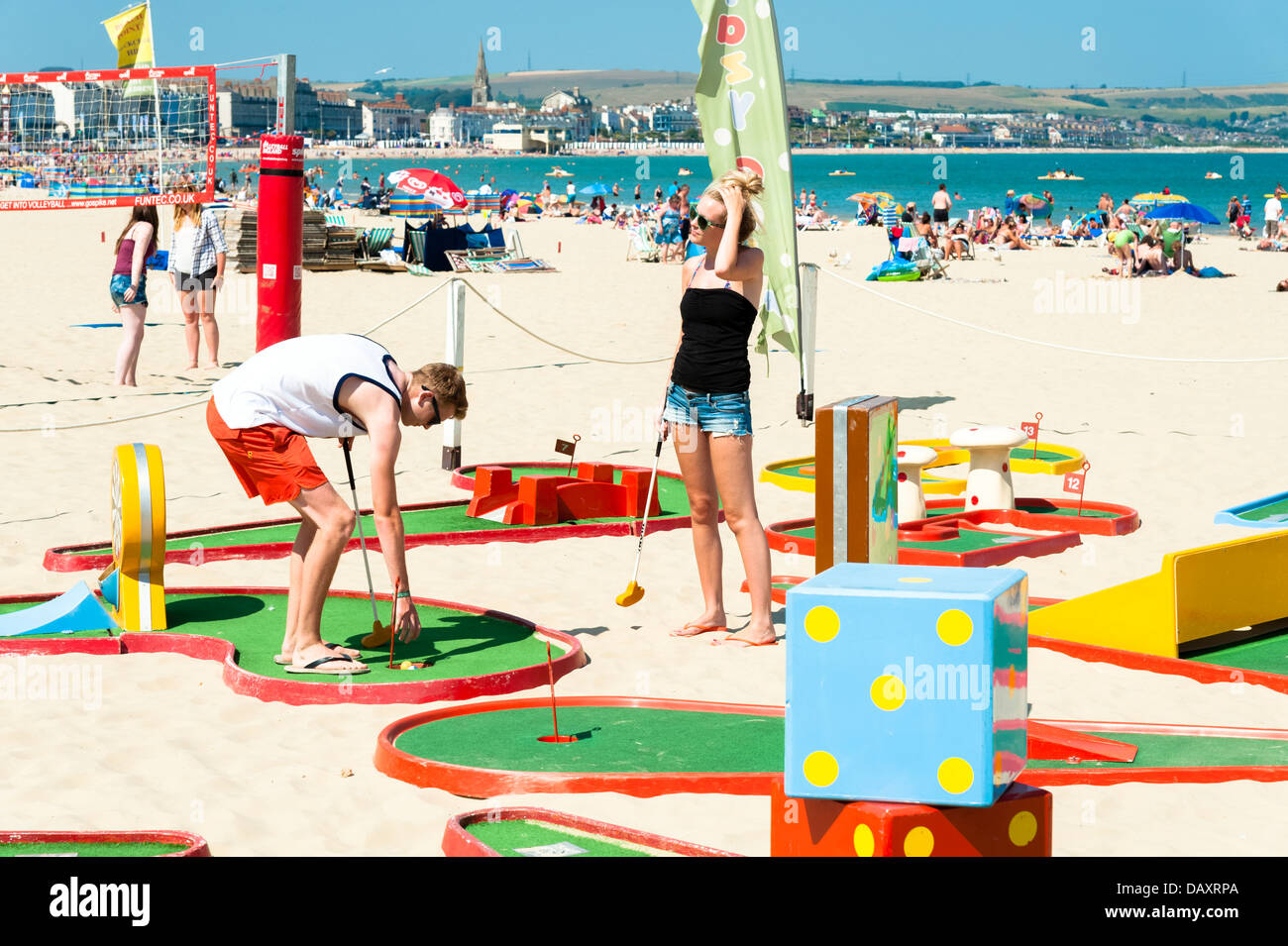 Young couple playing a game of crazy golf on the beach at Weymouth Bay, Dorset, UK. Stock Photo