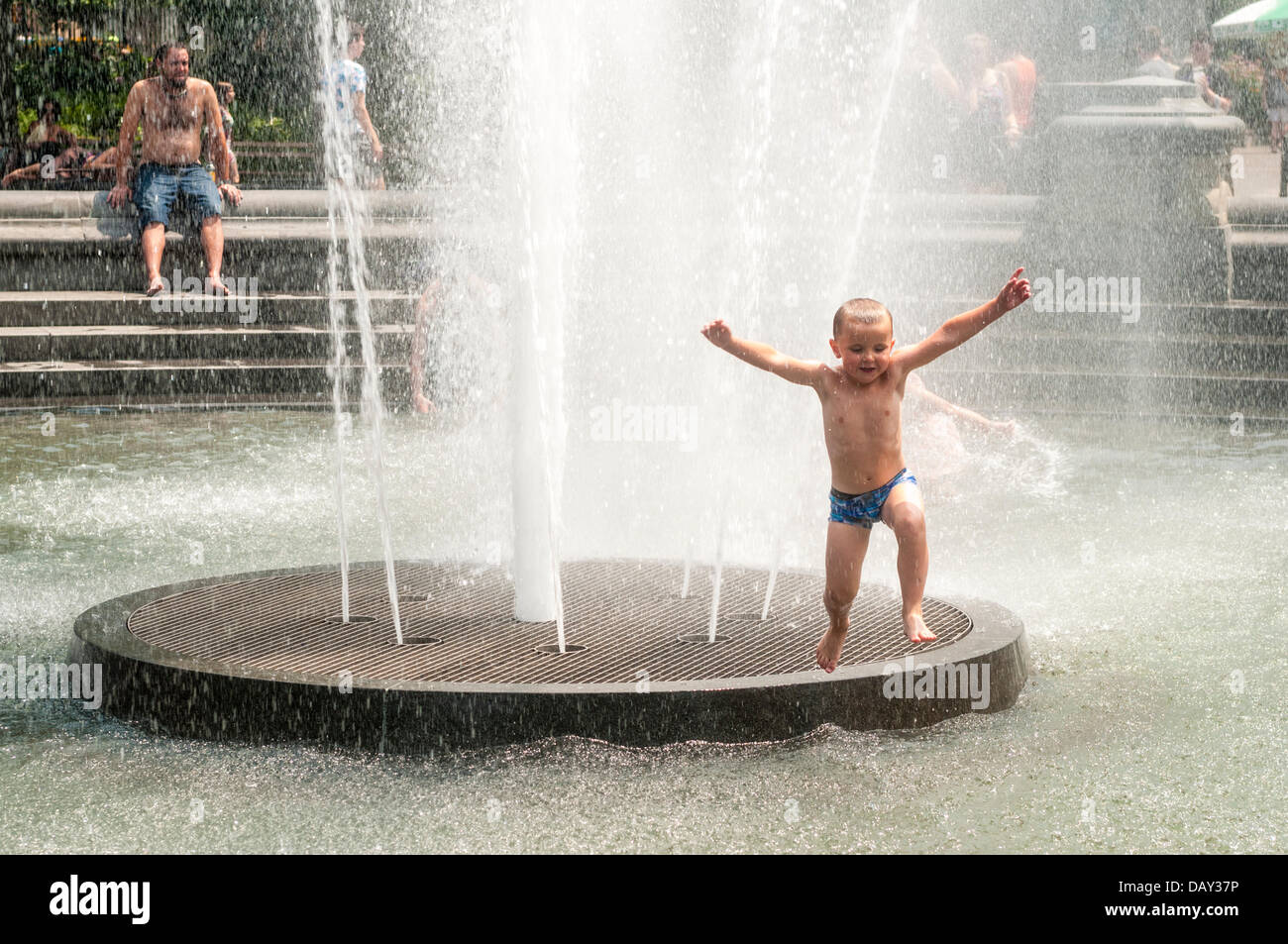 New York, NY 20 July  2013 - Summer heatwave, where temperatures have exceeded 90º farenheit, ( 33º Centigrade ) for the past week, a young boy frolics in the fountain in Washington Square Park.   On Thursday, electricity usage fell just short of an all-time high - 13,161 megawatts were used by 5 p.m., just 28 megawats fewer than a record set on July 22, 2011, Con Edison said, which lead to power outages on Staten Island. City officials urged New Yorkers to avoid exercising outdoors, drink plenty of water and check on any elderly neighbors. Stock Photo
