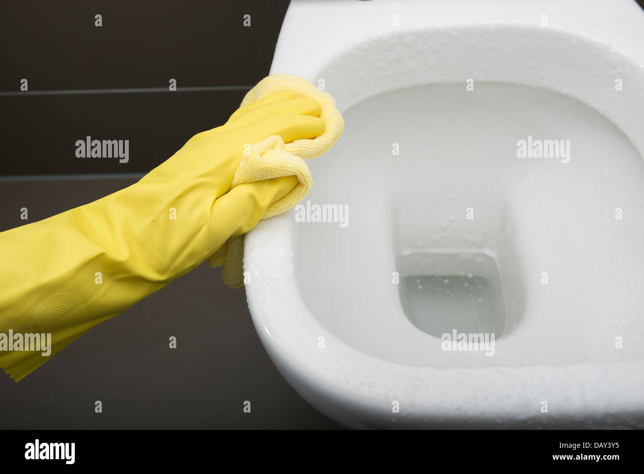 Hand wearing yellow Rubber Glove cleaning a modern white toilet with a