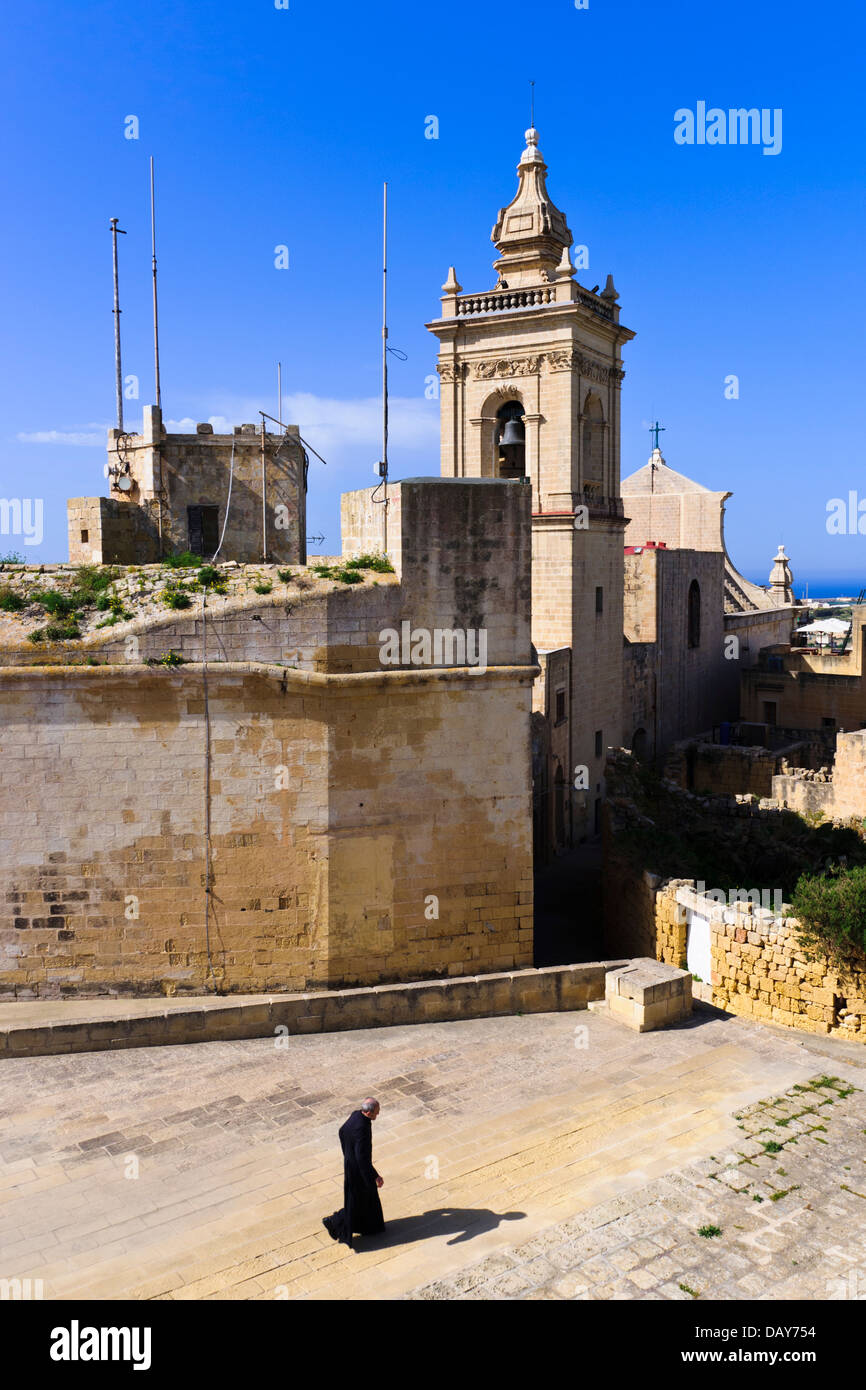 A friar walks in front of the Cathedral of the Assumption in the old citadel of Victoria (Rabat), Gozo, Malta. Stock Photo