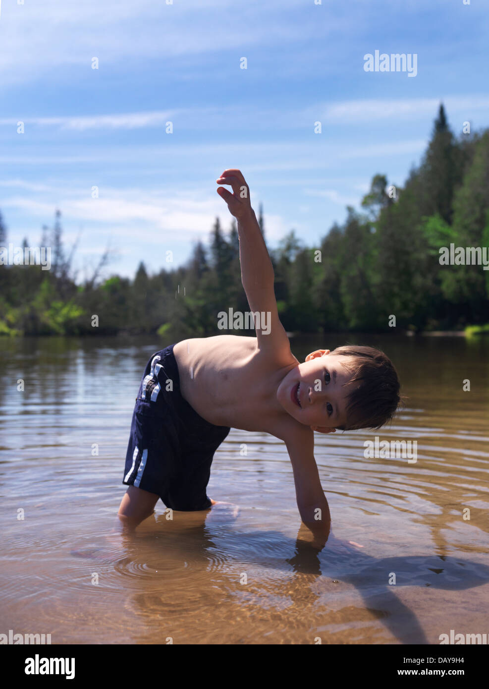 Portrait of a happy smiling child, 3 year old boy, playing in lake water in the nature. Ontario, Canada. Stock Photo