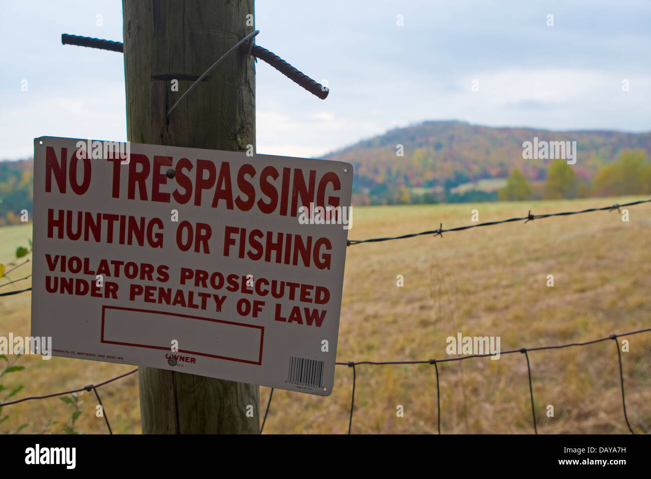 No Tresspassing sign on a fence with barbed wire in front of a field and mountain, Virginia, United States of America Stock Photo