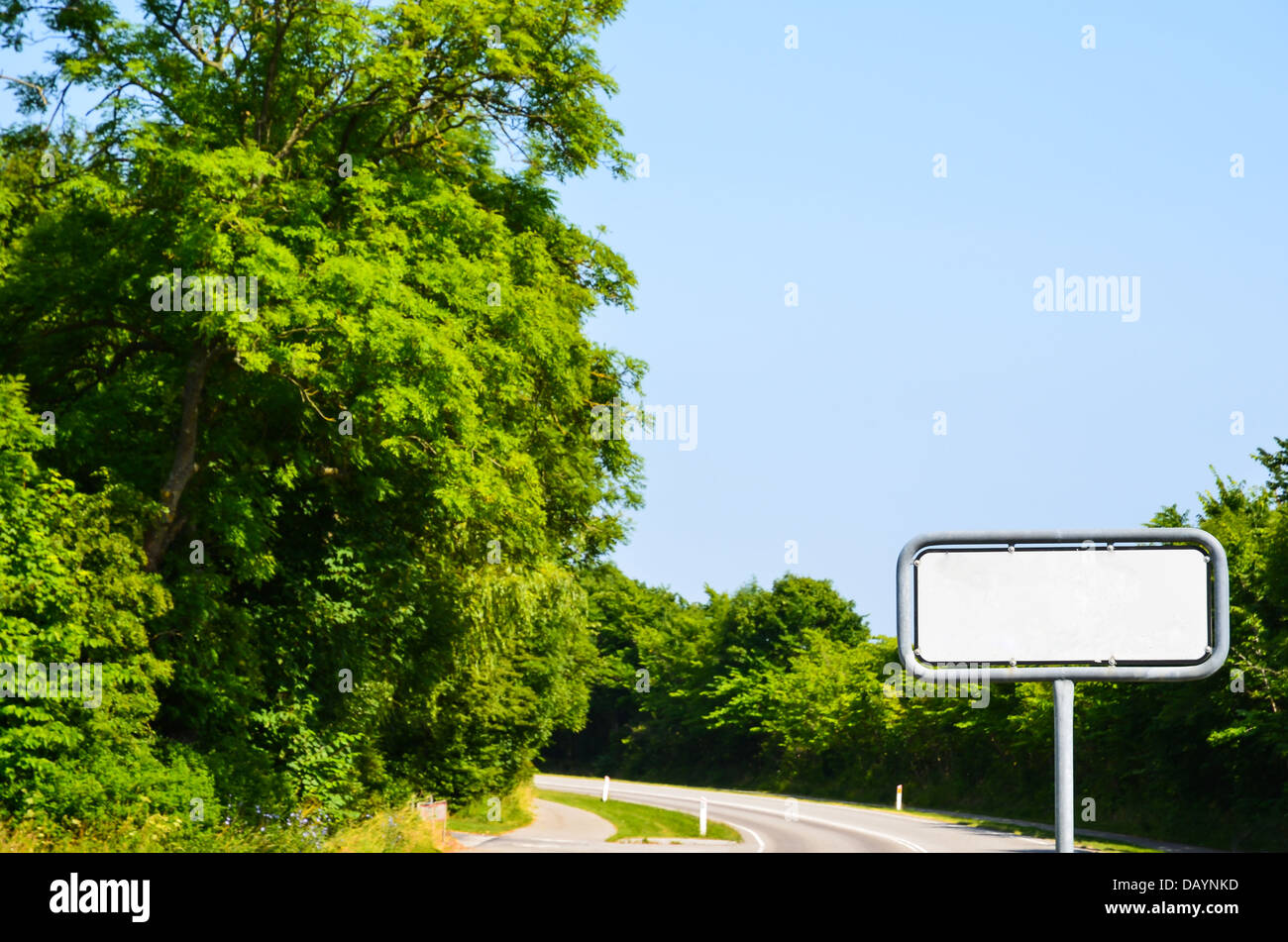 Blank road sign at a road with green trees Stock Photo - Alamy
