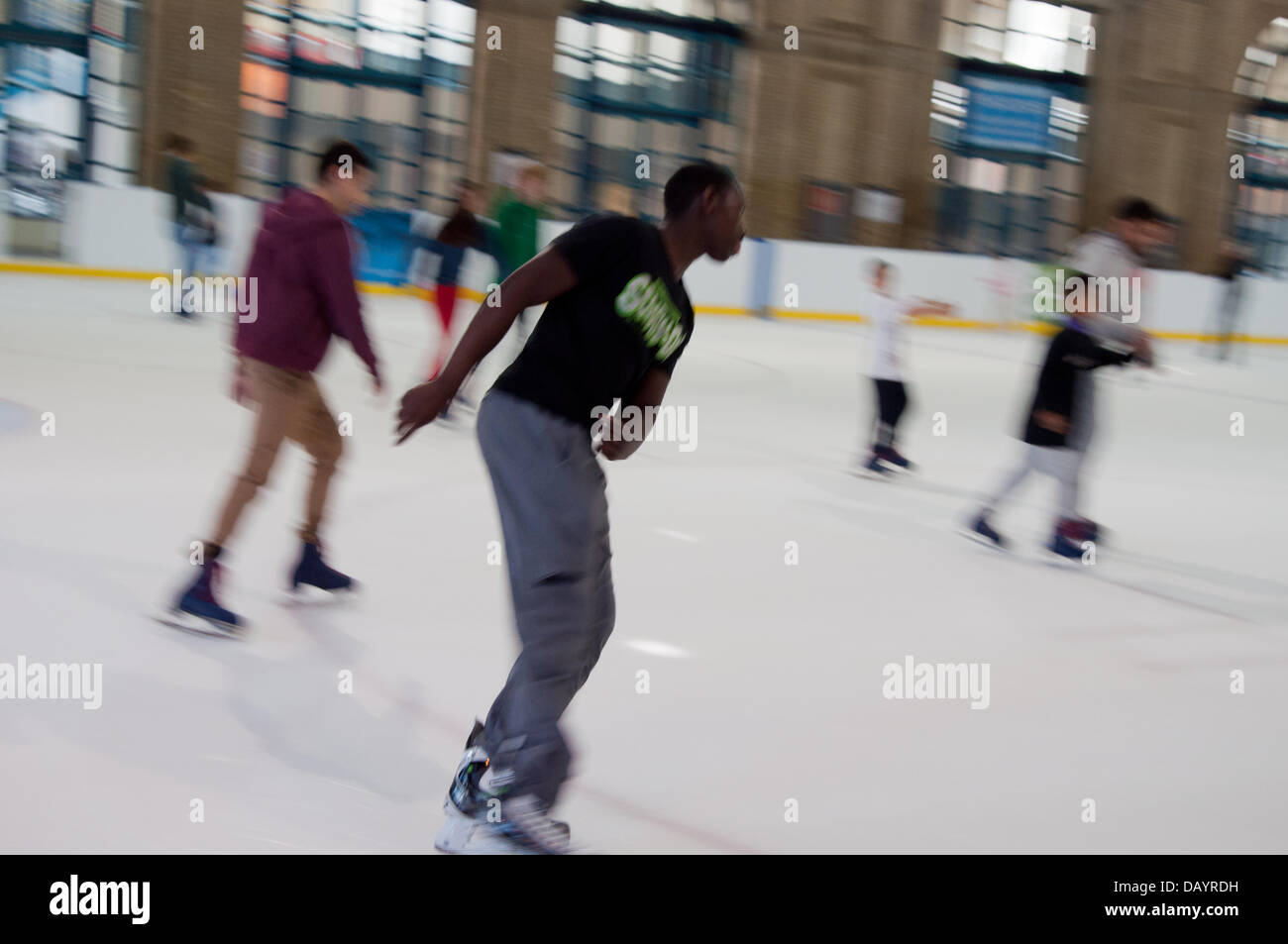 A young black male skater speeds round Alexandra Palace Ice Rink, with