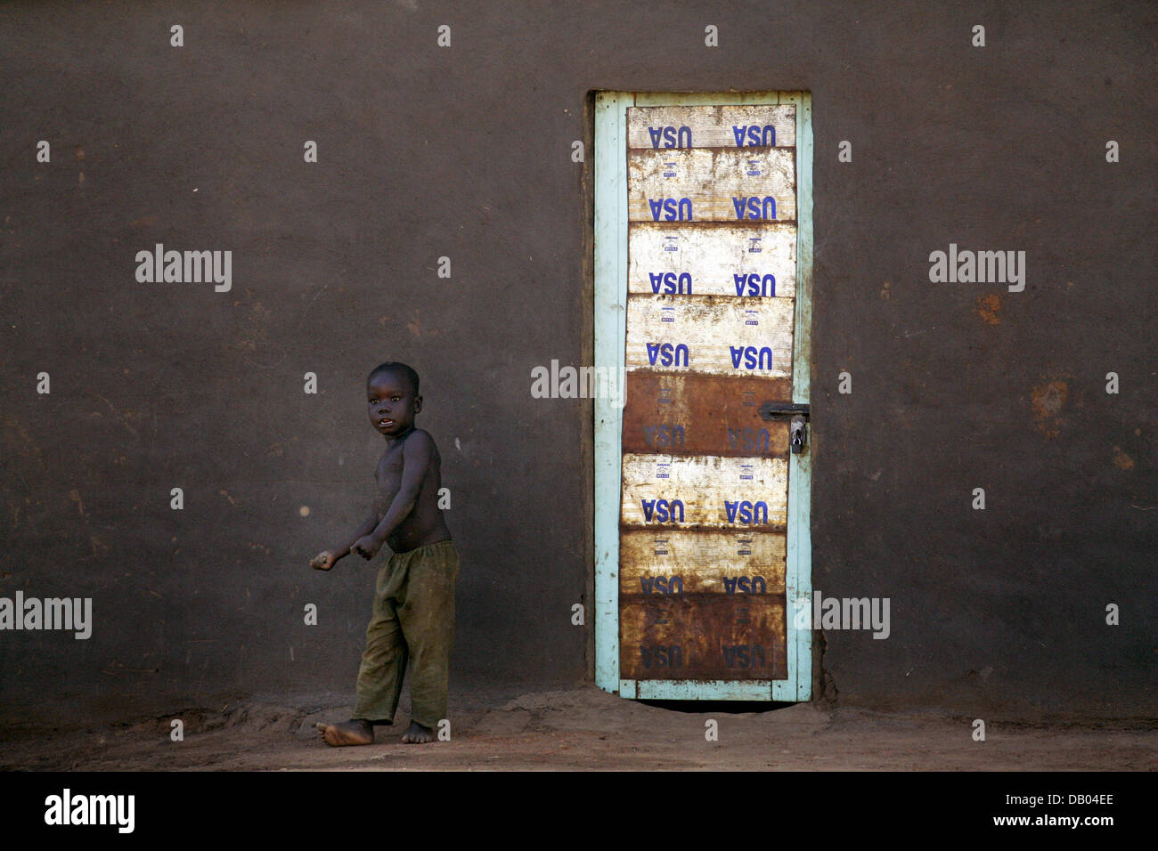 A Child Plays Near A Rusty Door Made Of Tin Cans From The Us