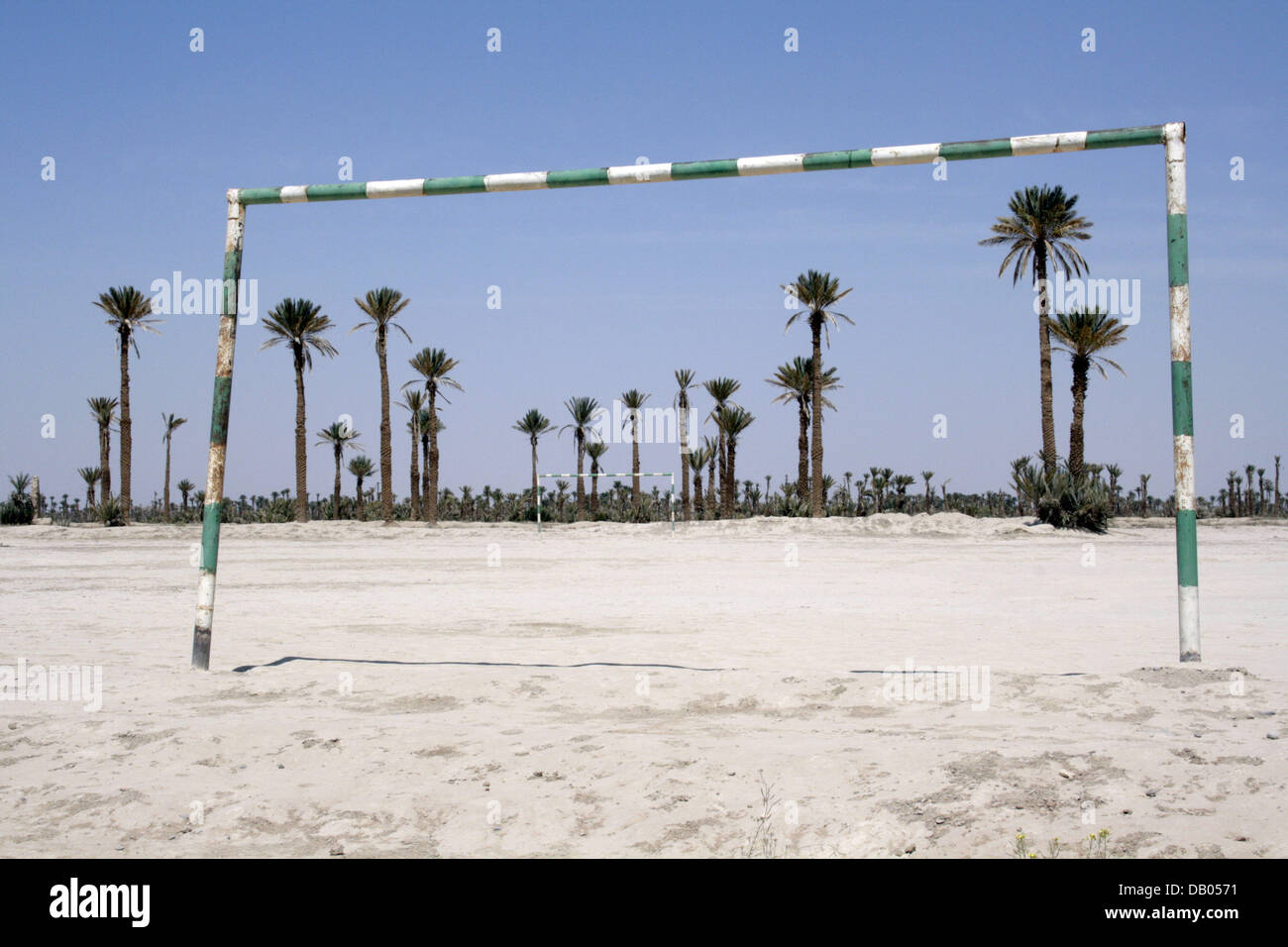 A football ground out of sand instead of grass is surrounded by palms ...