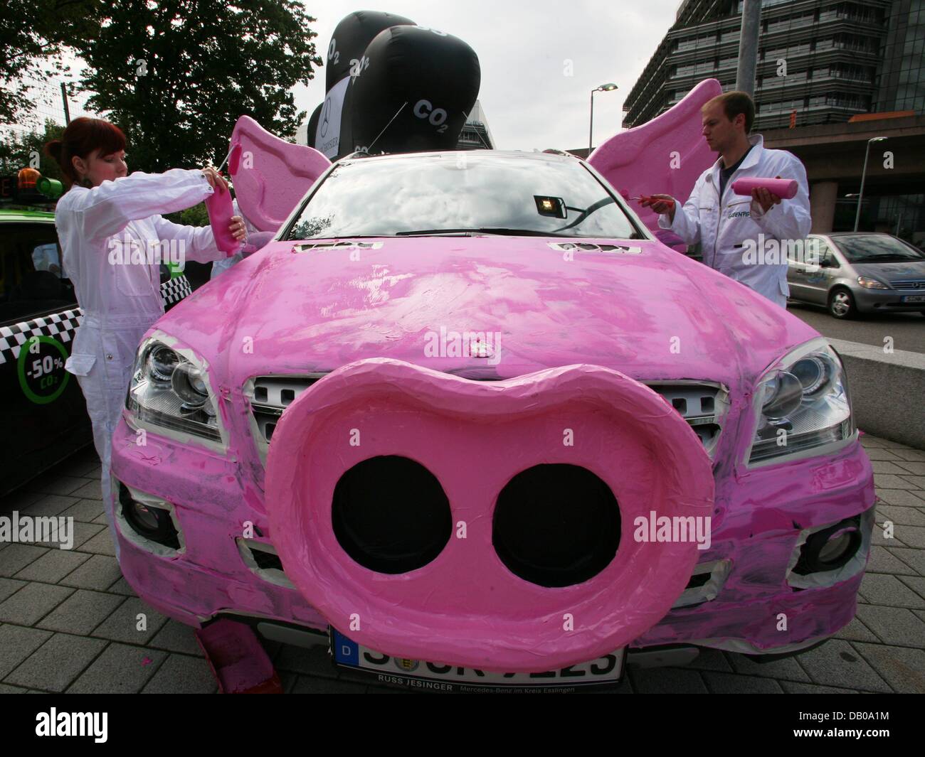 Members of environmental protection organisation 'Greenpeace' prepare a protest campaign against climate-damaging policies of automobile manufacturer DaimlerChrysler in front of the Mercedes-Benz museum in Stuttgart, Germany, 25 July 2007. For this purpose the campaigners paint two Mercedes cars in pink and decorate them with snouts and ears to symbolise pigs. Giant balloons stand  Stock Photo