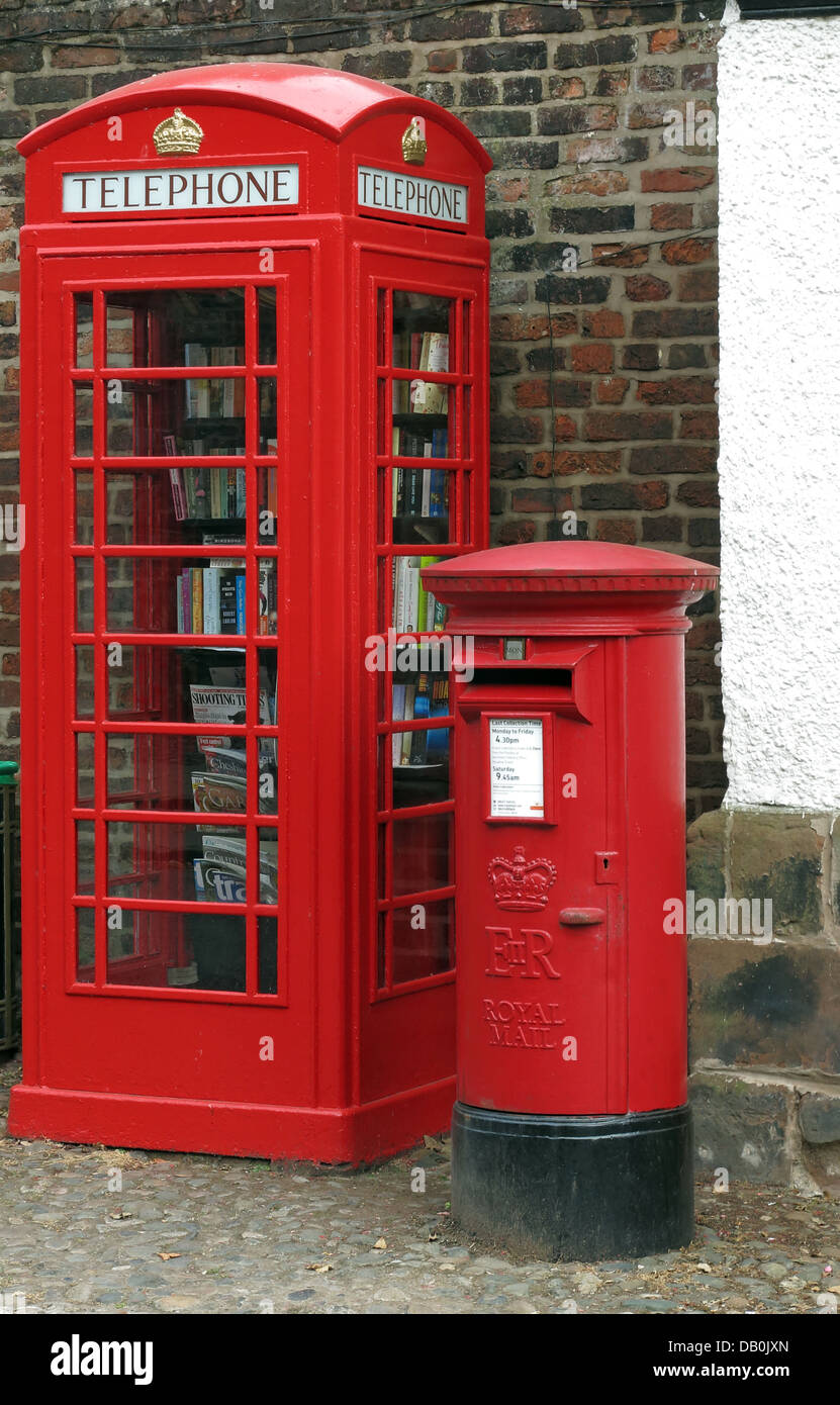 An old red British Telephone box turned into a British village eccentric lending library , next to a working post / pillar box Stock Photo