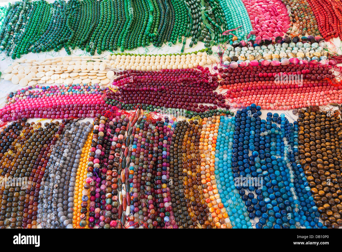 Colorful craft jewels and straw hats on sale. Hanging plastic and glass  souvenir necklaces at local market. Otranto, Italy. Stock Photo