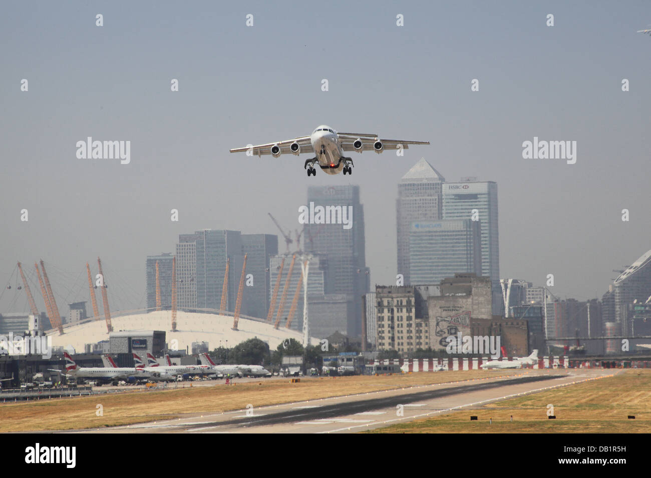 A British Aerospace 146 jet takes off at London City Airport with Canary Wharf and the Millennium Dome in background Stock Photo