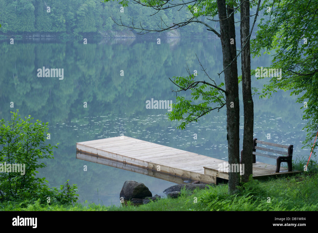 A dock and the far shore are reflected in the mirrored surface of a lake Stock Photo