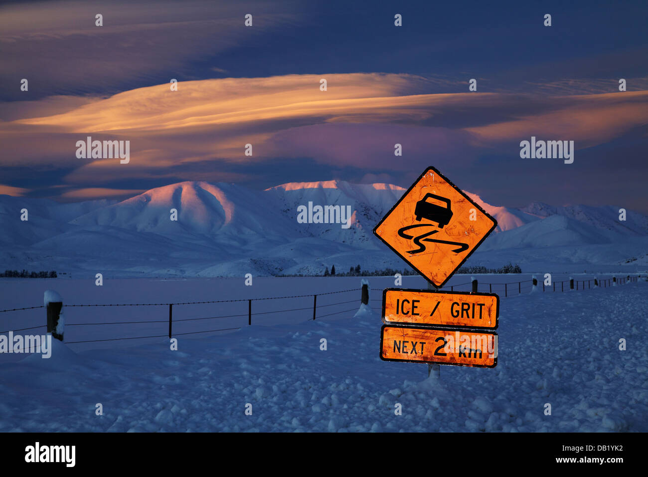 Icy road warning sign and alpenglow on Hawkdun Range, and lenticular clouds, Maniototo, Central Otago, South Island, New Zealand Stock Photo