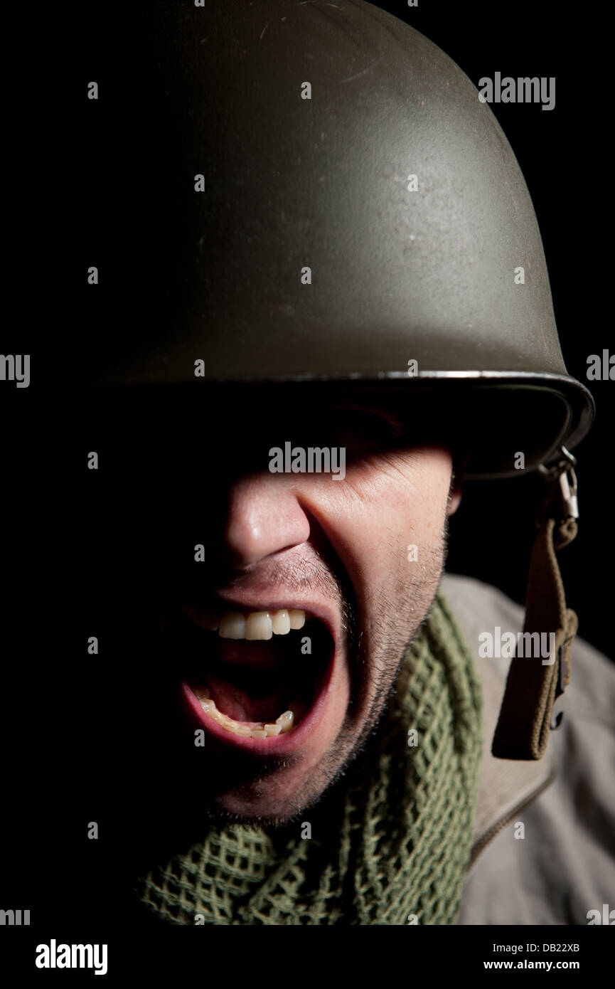 Spotlit portrait of a screaming/shouting American WW2 soldier against a black background with eyes in shadow. Stock Photo
