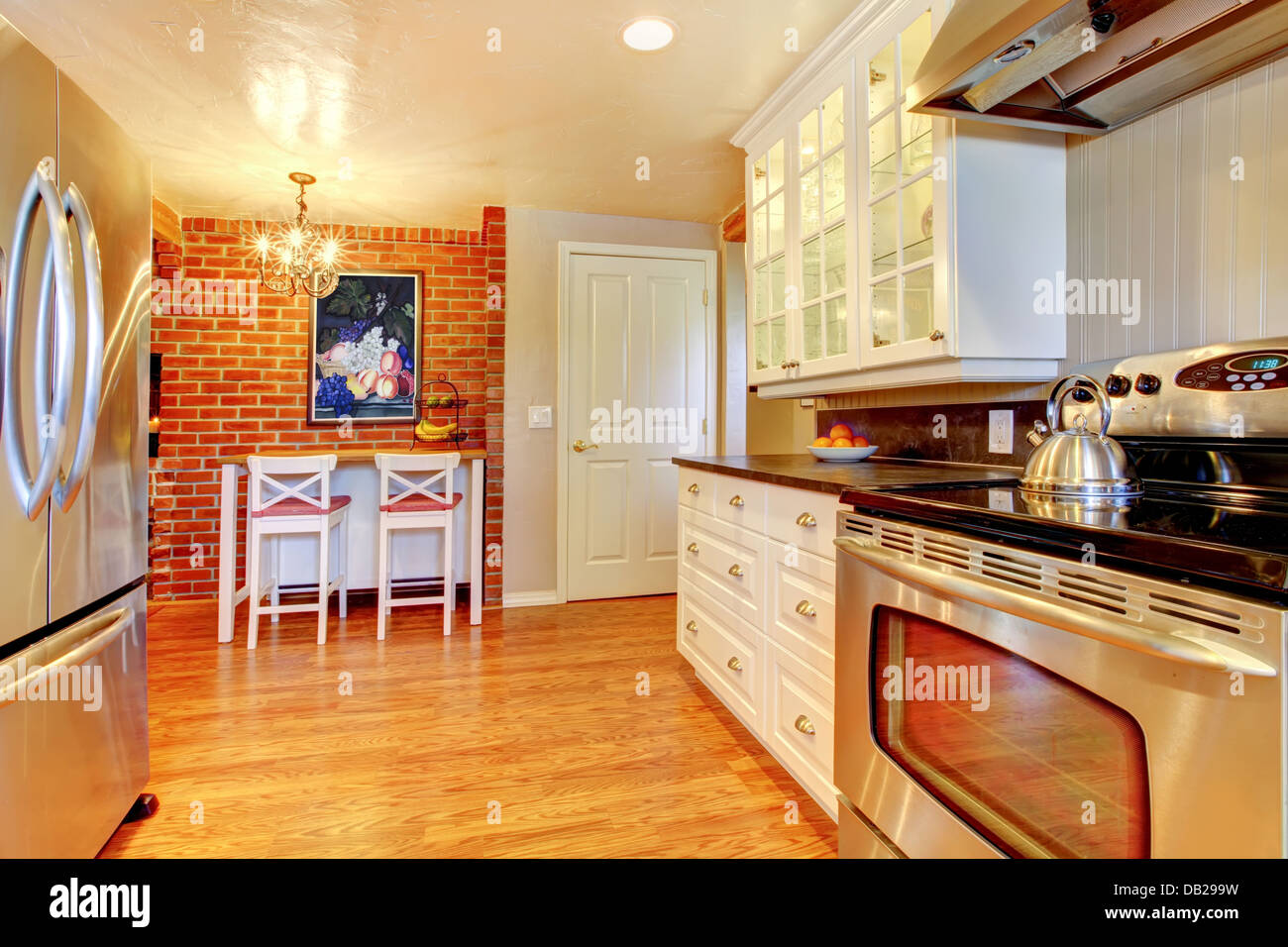 White kitchen with brick wall, hardwood and stainless steal stove. Stock Photo