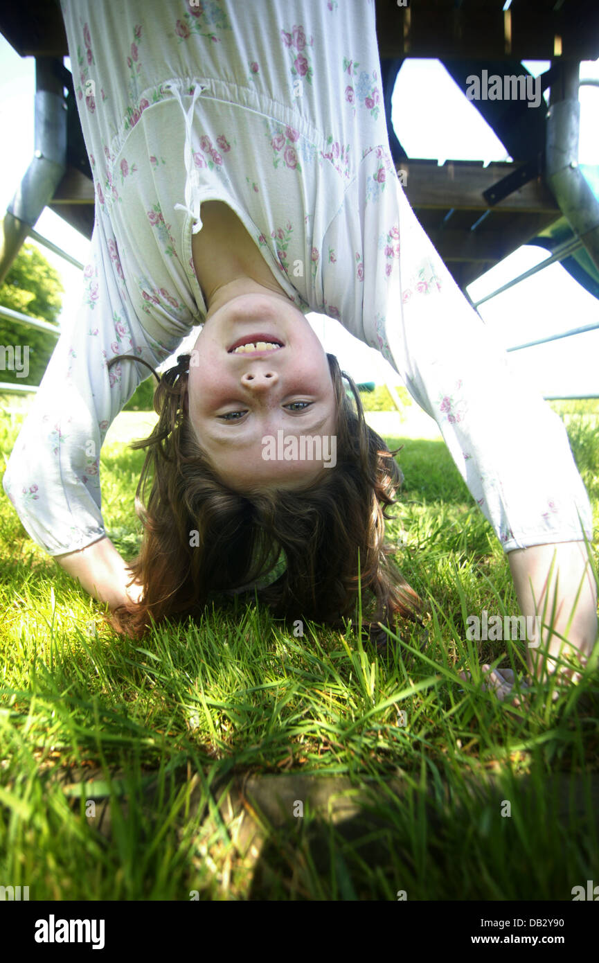 small female child hanging upside down whilst playing in her own garden Stock Photo