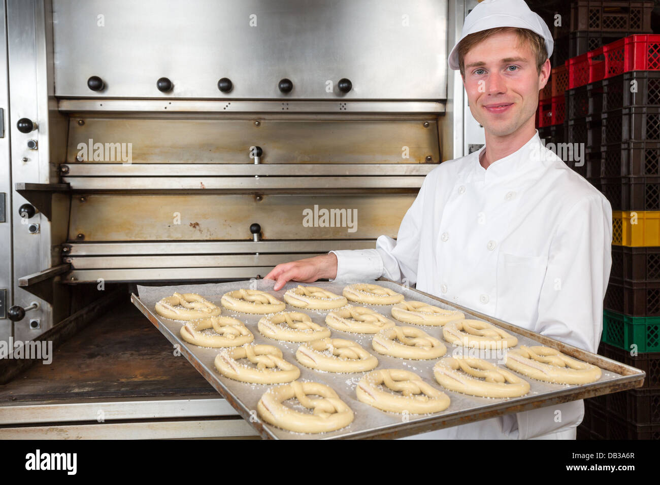 Baker in bakehouse or bakery presenting baking plate with pretzel dough Stock Photo